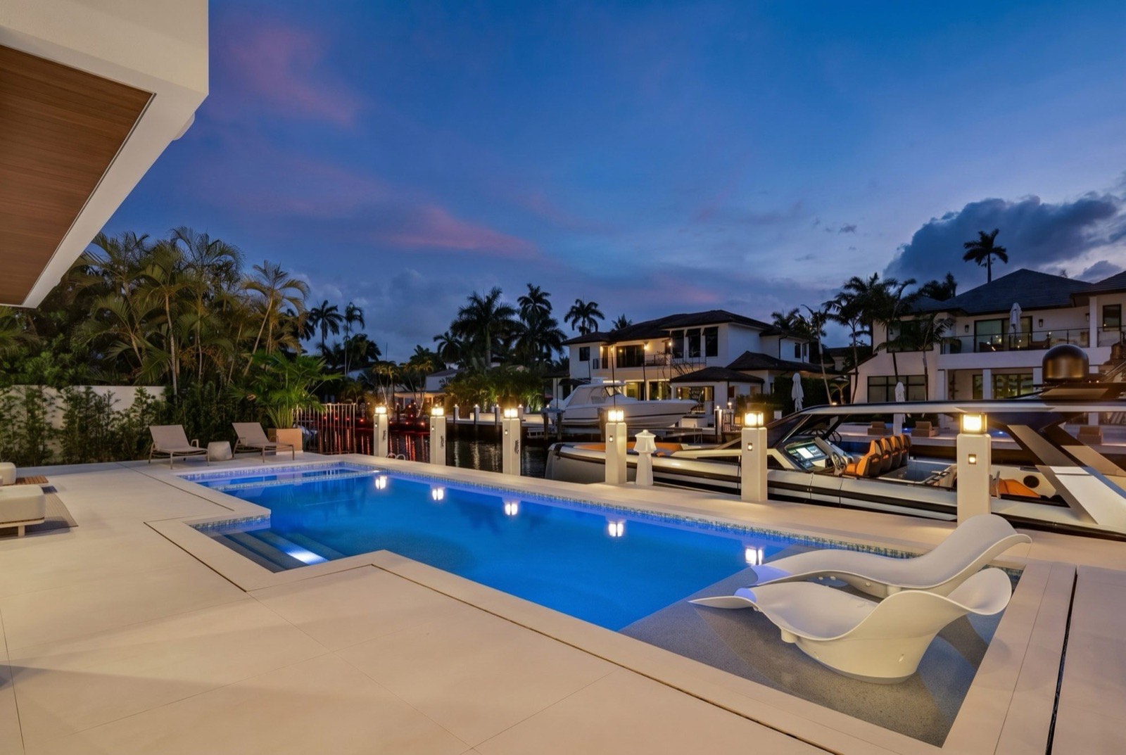 Rear elevation of the residence from the canal at dusk, with lit terraces, pool, and dock